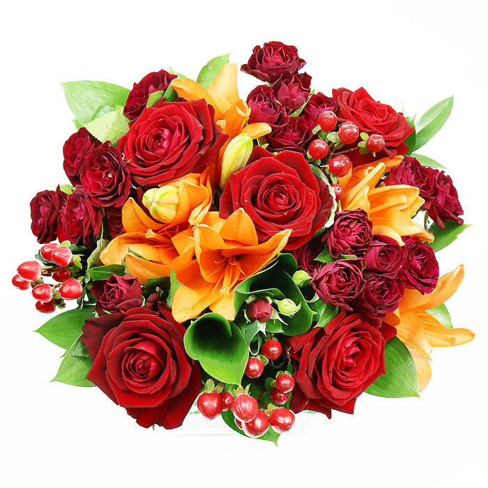 Captured from above on a clean white plane, this densely packed circular bouquet reads as a deliberate composition of warm tones and contrasting textures. Large, fully bloomed deep red roses assert themselves visually, their layered, velveteen petals opening wide to reveal shadowed centres and a classic perfume that suggests intimacy and long-held affection. Interspersed among them are vivid orange Asiatic lilies - some trumpet-shaped flowers display their stamens and subtle dark speckling, while nearby buds and partially opened blooms introduce movement and promise. Smaller, dark burgundy spray roses are clustered throughout, offering concentrated jewel-coloured depth and a plush, compact texture that complements the larger roses. Small clusters of glossy red Hypericum berries appear like scattered garnets, reflecting light and providing a crisp, rounded texture against the softness of the petals. Fresh, broad green foliage resembling ruscus or salal slips in between blooms, its glossy, slightly leathery leaves balancing the palette with cool, verdant notes and framing the bouquet's edges. The photographer's soft, even lighting emphasizes the tactile contrasts - the satiny lily faces, the matte velvet of roses, and the firm sheen of berries - without casting harsh shadows, making the arrangement readable to the eye and evocative to the imagination. Sensory details linger: the deep rose scent tempered by a citrus-spicy undercurrent from the lilies. The overall impression is opulent yet approachable - ideal for marking anniversaries, autumn celebrations or as a romantic delivery to a house near Bickley Park or along Widmore Lane - a piece that feels both classic and freshly made by a knowledgeable local florist.