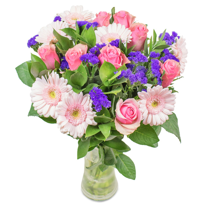 A vibrant bouquet, elegantly arranged by Flowers Bickley and presented in a slender clear glass vase, stands out against a pristine white setting. The composition features approximately seven to nine medium pink roses, each with petals still furled or just beginning to unfurl, their classic spirals reminiscent of rose gardens off Southborough Road. Surrounding them are five to seven pale pink gerbera daisies, their large, round heads and faintly lighter centres evoking the gentle warmth of Bickley summer mornings. Scattered throughout, bright purple statice blooms create dynamic contrast and texture, adding a pop of deeper colour to the soft pink theme. A base of glossy, deep green foliage infuses the bouquet with abundant freshness and vibrancy, echoing the thriving local parks. Visible stems submerged in the clear vase emphasize the bouquet's just-picked vitality, as you would expect from a fresh flower delivery in Bickley. Perfect for celebrating a birthday, honoring a special anniversary, brightening Mother's Day, or adding a cheerful accent to a Bickley home or office, the arrangement radiates joy, affection, and artisanal care rooted in the heart of the community.